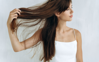 Mulher de blusa branca segurando com uma mão seu cabelo liso