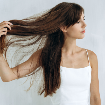 Mulher de blusa branca segurando com uma mão seu cabelo liso