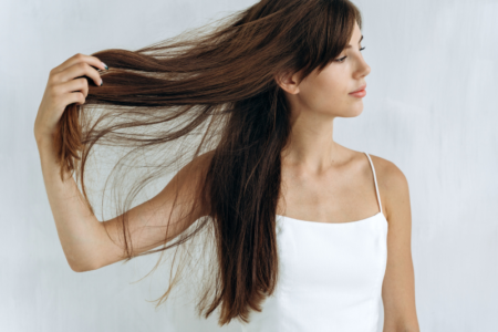 Mulher de blusa branca segurando com uma mão seu cabelo liso